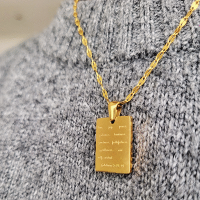 Fruit of the spirit necklace in gold tone over a grey jumper
